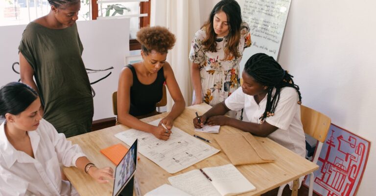 Cinco mulheres em uma mesa, discutindo e trabalhando em projetos criativos