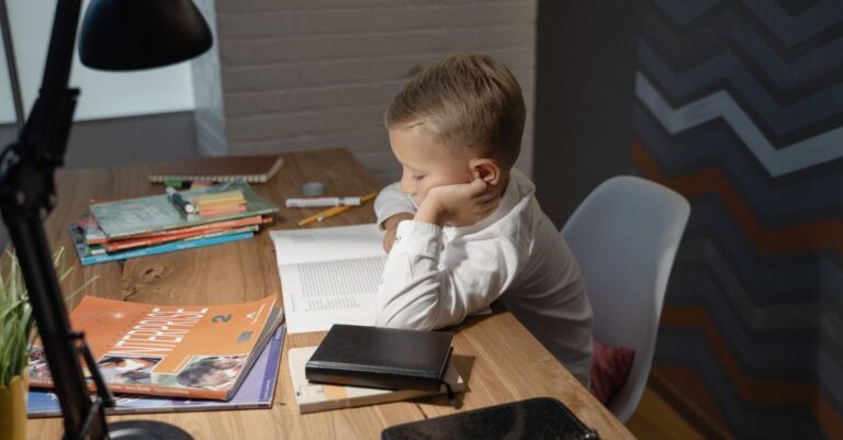 Alfabetização 7 anos: quais habilidades de leitura e escrita devem ser trabalhadas? Menino concentrado lendo um livro em uma mesa de estudos